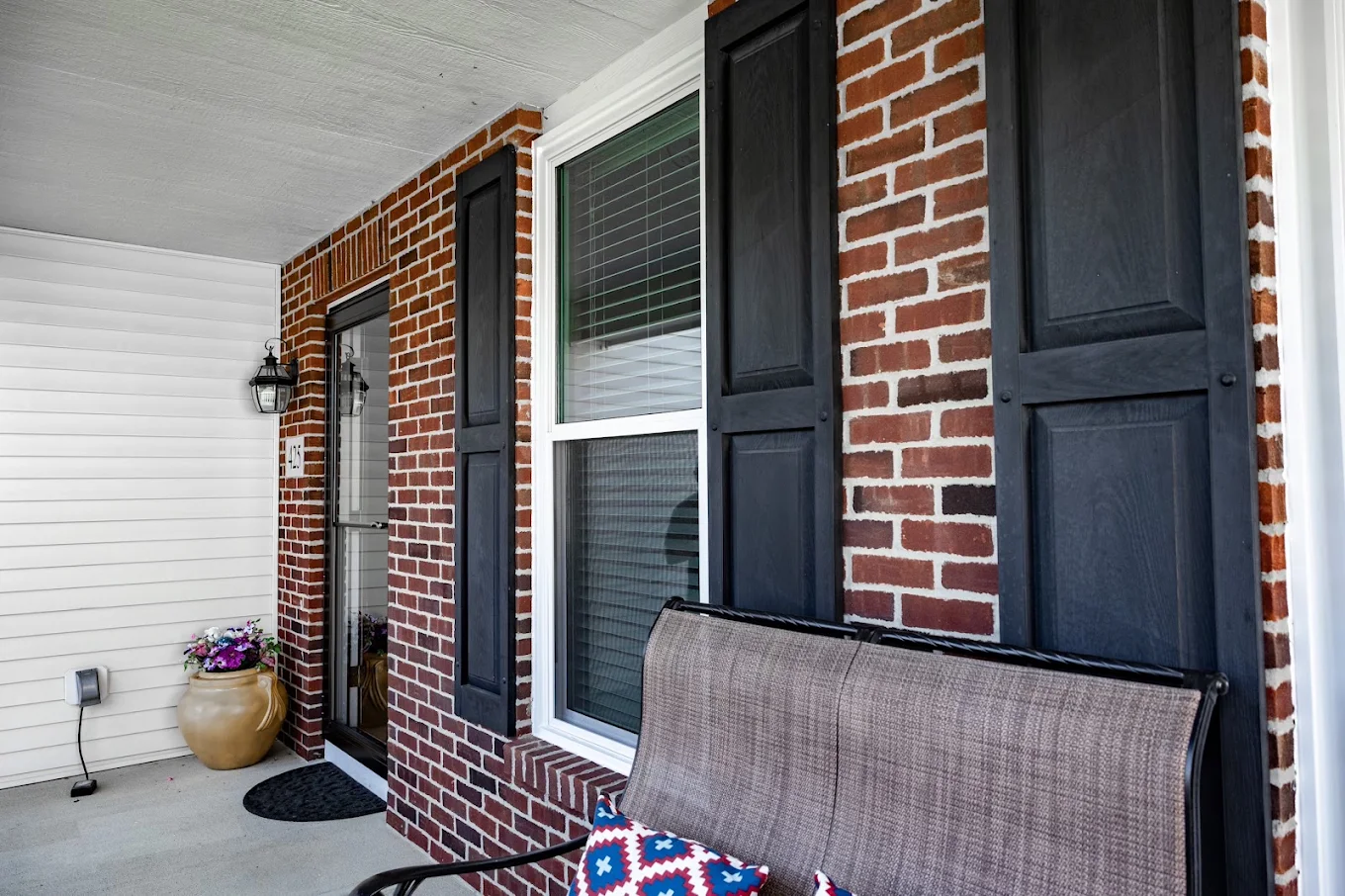 Custom double-hung replacement window with black shutters installed on a brick front porch by Zion Windows in Columbus, OH